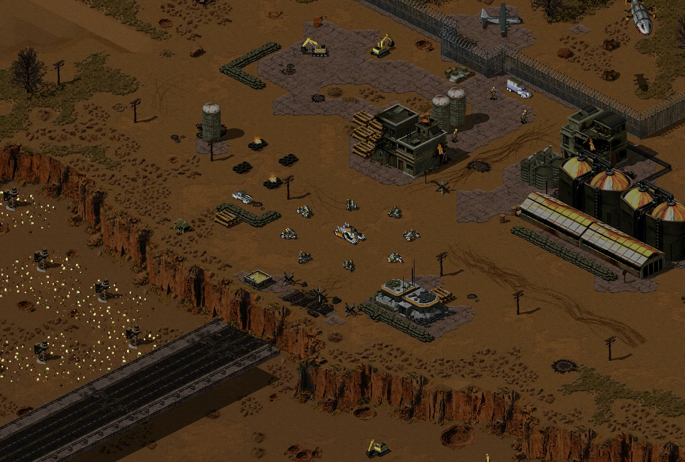 Izometryczny widok pustynnego pola bitwy z pojazdami wojskowymi, budynkami i umocnieniami z moda C&C: Battlegrounds