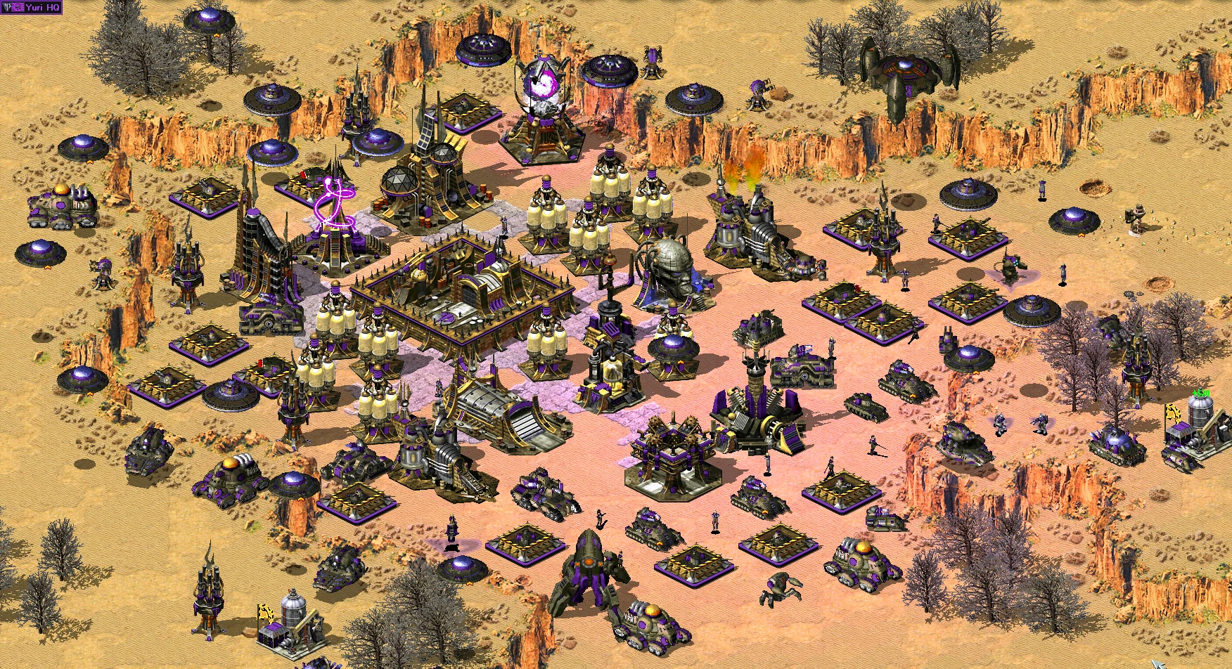 Zrzut ekranu z moda Reboot do Command & Conquer Yuri's Revenge przedstawiający mocno ufortyfikowaną fioletową bazę z budynkami, obroną i jednostkami na pustynnym terenie
