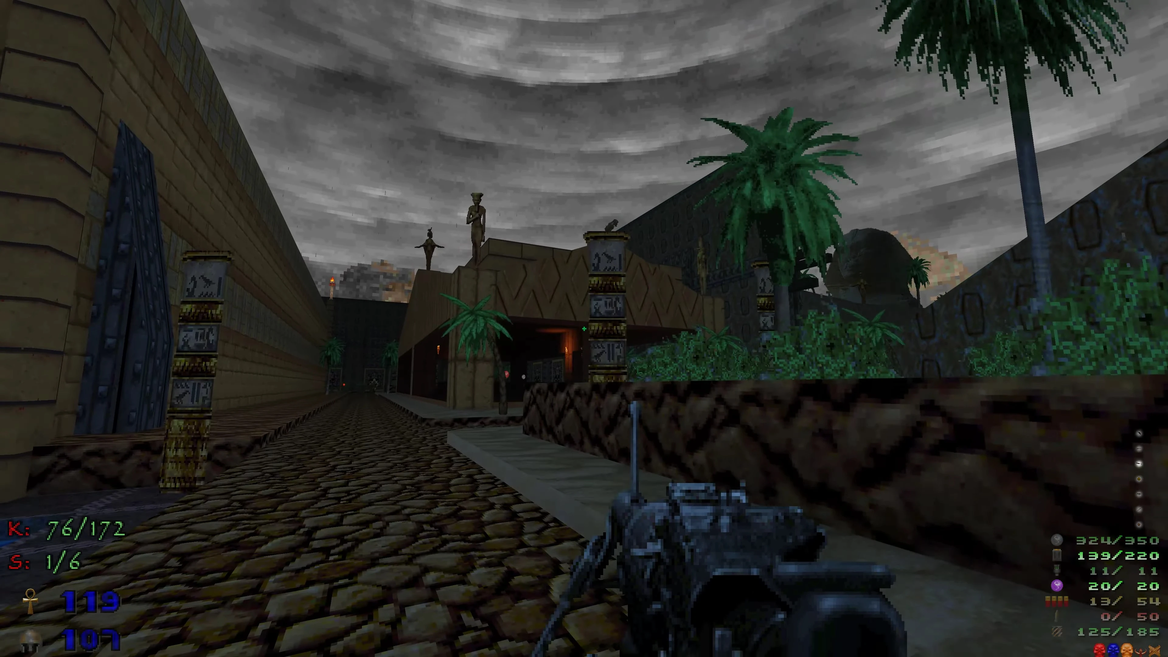 Gameplay screenshot showing a weapon in hand and an ancient Egyptian style courtyard with statues and palm trees under cloudy sky