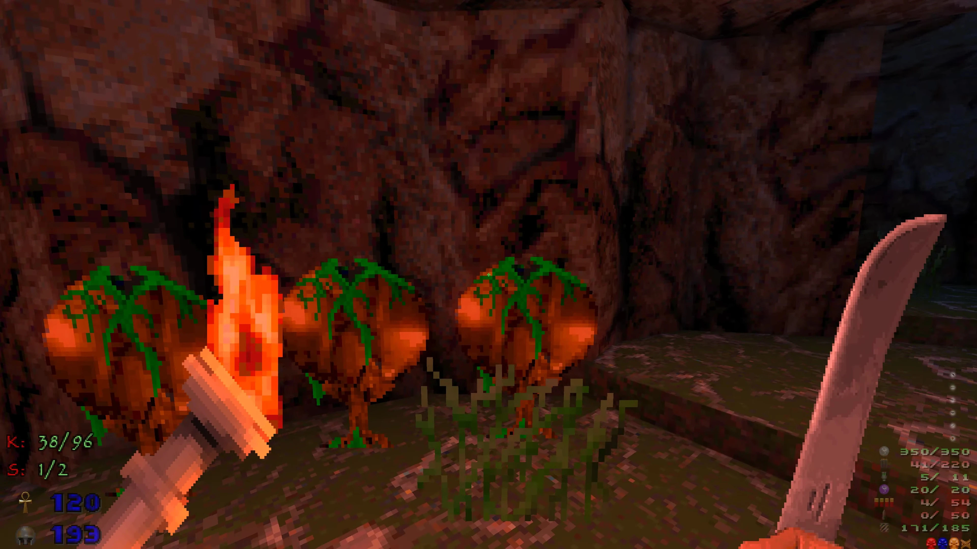 First-person view holding a burning torch and machete in a dark rocky cave with pixelated orange plants