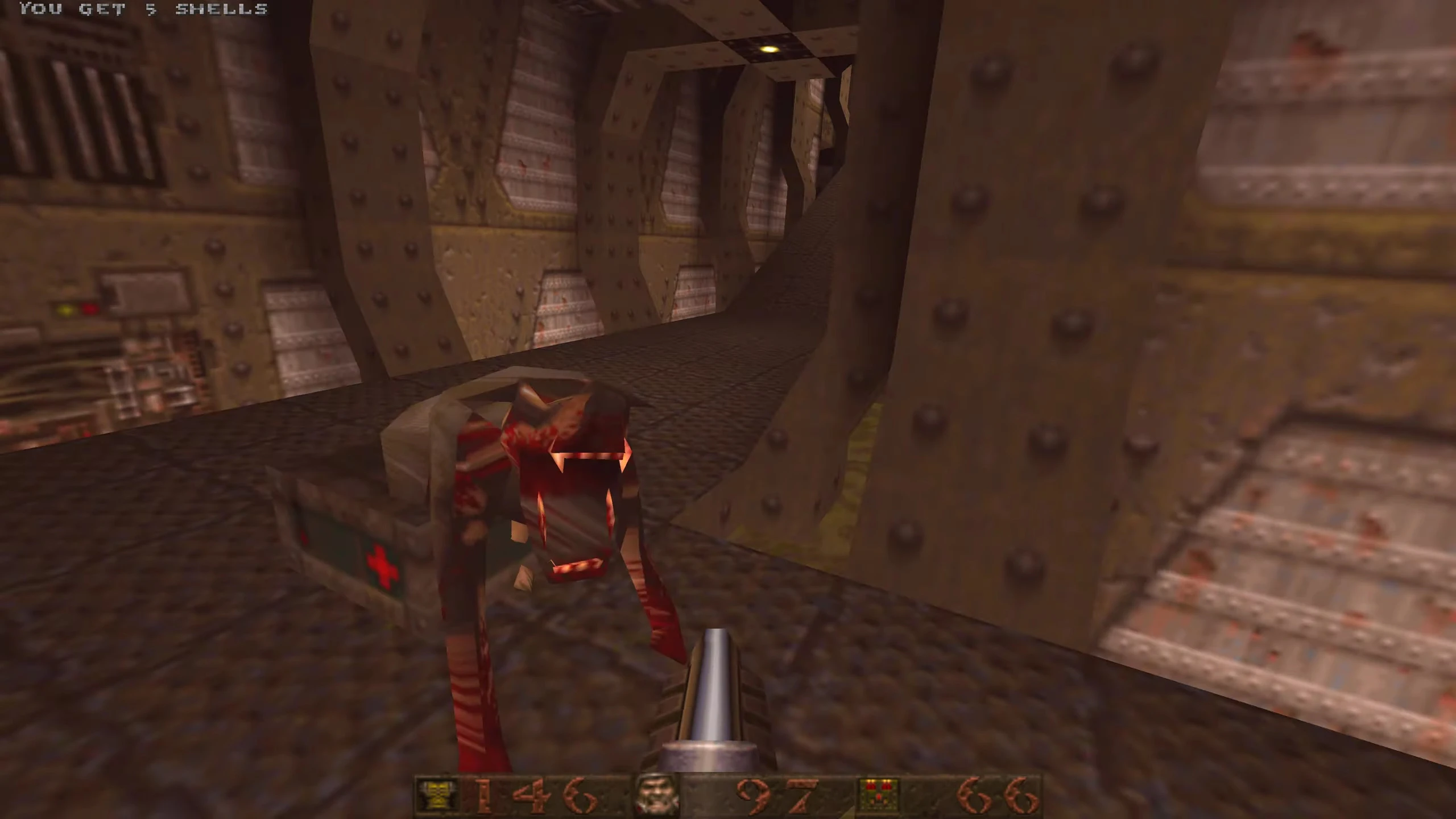 First-person view in Quake 1996 showing player aiming shotgun at a monster in a rusty metal corridor