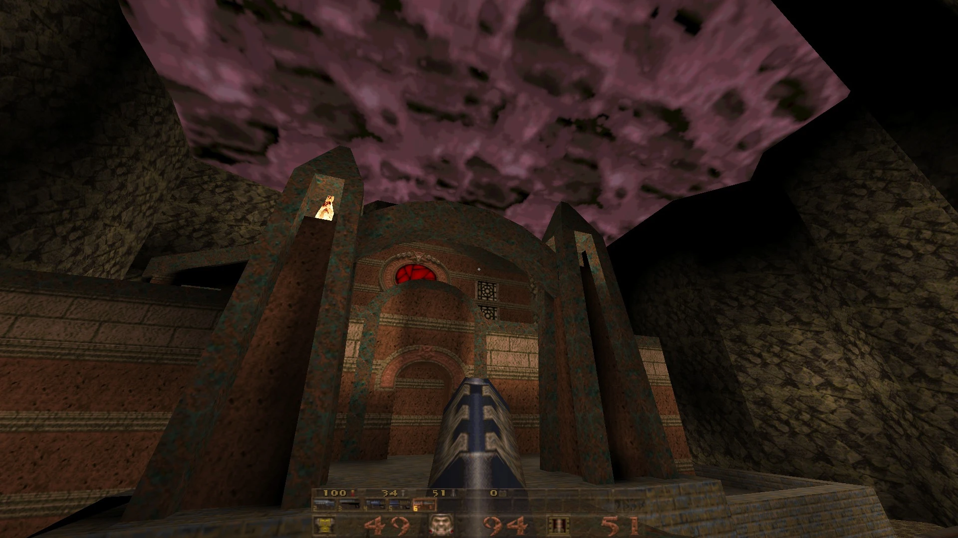 View of a dark stone fortress with rusted metal arches and a red sky backdrop in Quake via QuakeSpasm engine