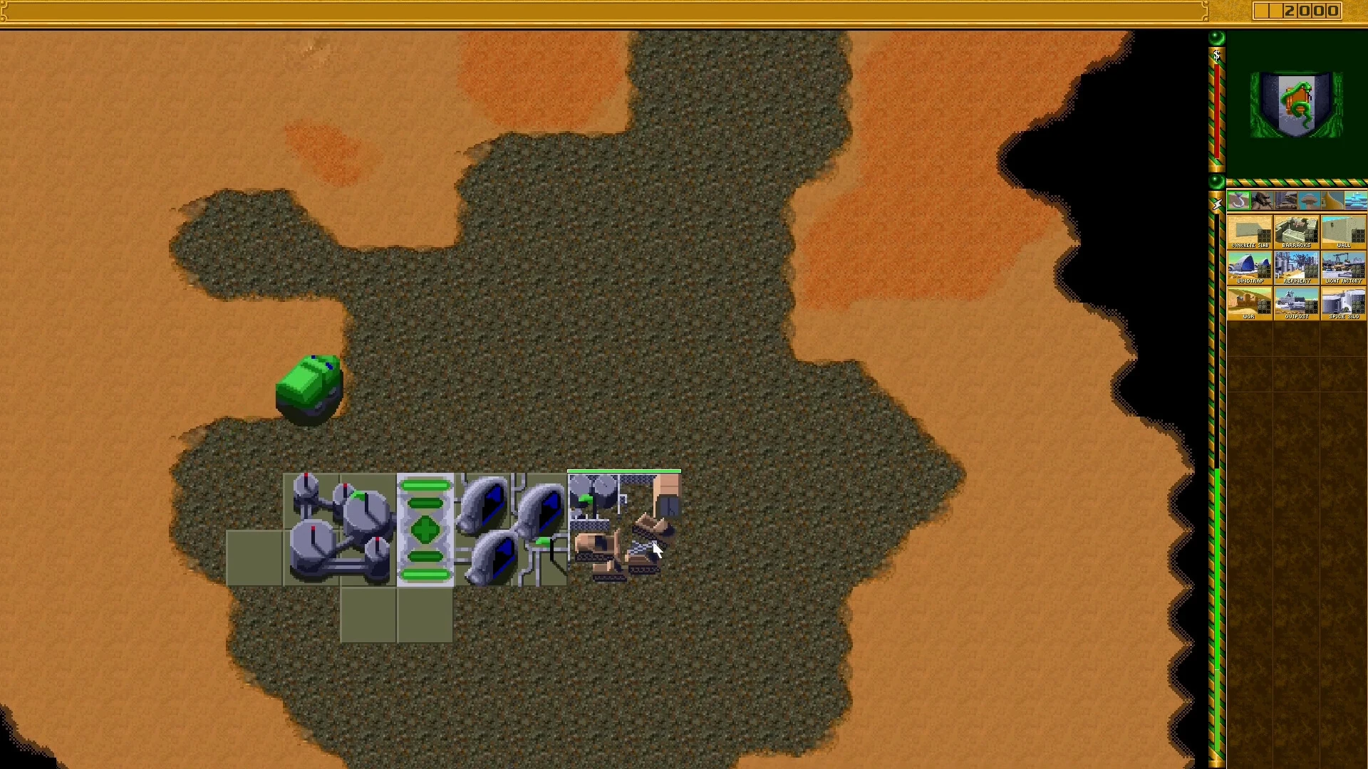 Draufsicht auf Basisstrukturen und eine grüne Einheit auf Wüstenboden in Dune II The Maker