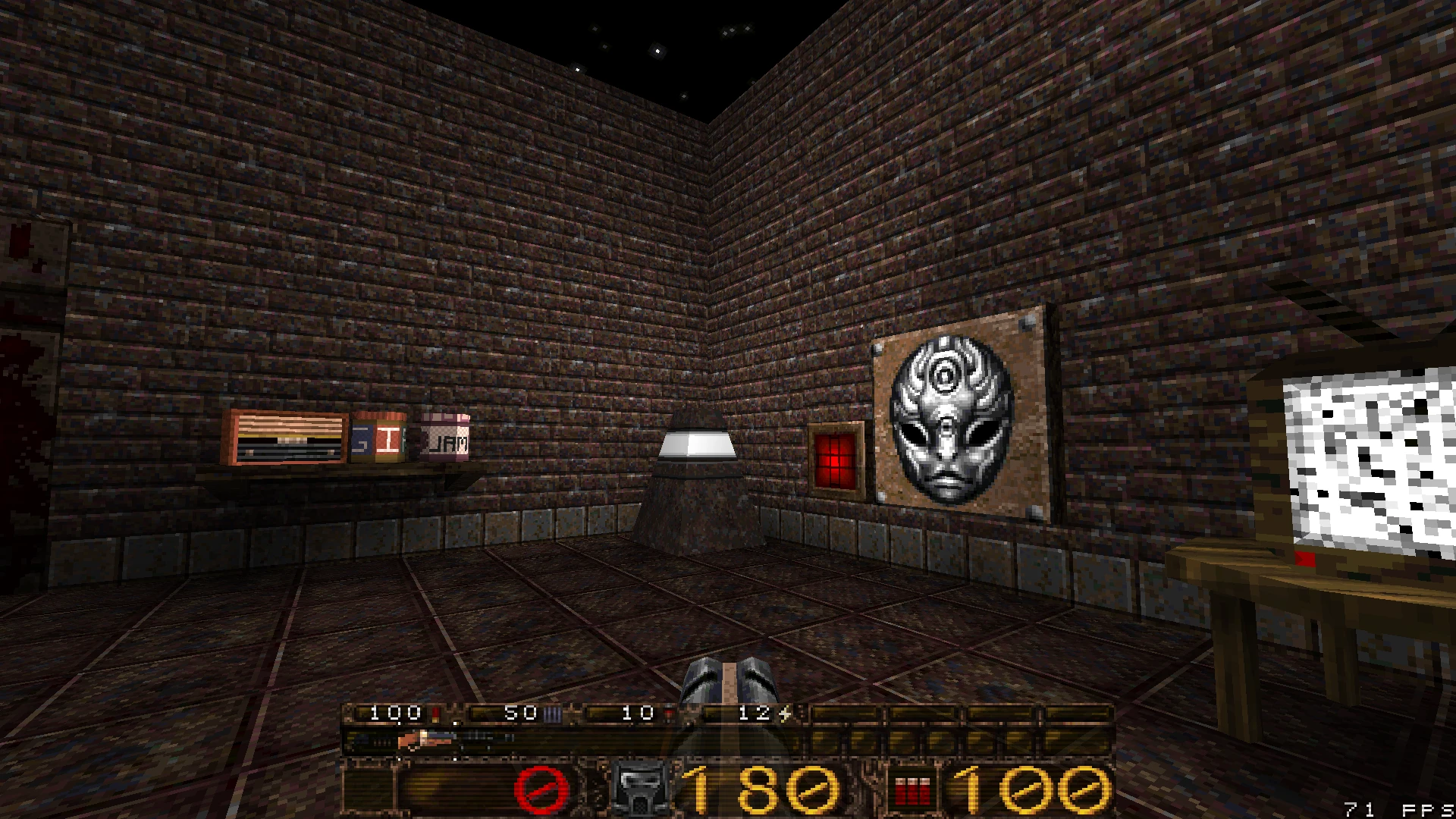 Zrzut ekranu gry ukazujący ciemny pokój z cegły z półkami, maską na ścianie i retro telewizorem w LibreQuake