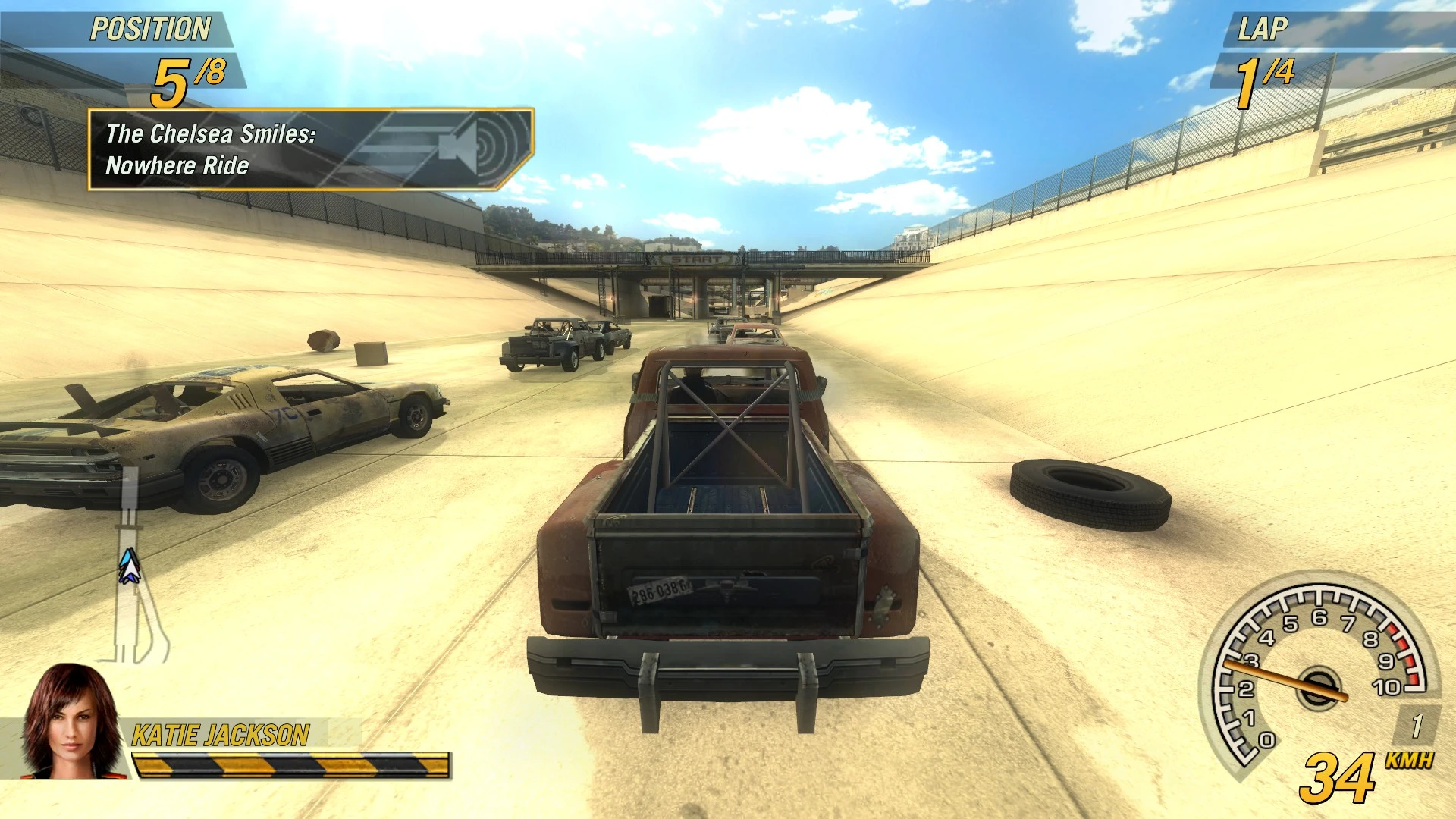 Captura de pantalla de FlatOut 2 con camión oxidado y coches dañados compitiendo en un canal arenoso iluminado por el sol