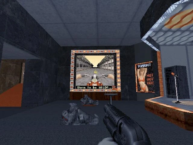 Vista en primera persona en Duke Nukem 3D con escopeta, dos enemigos caídos y pantalla arcade con juego de motocicleta