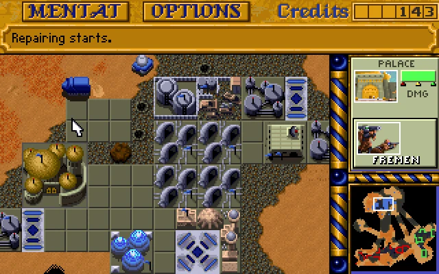Top-down view of a Dune II desert base with buildings, pipes, and a cursor over the terrain