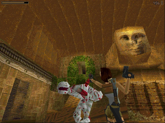 Lara Croft dispara a una momia manchada de sangre dentro de una cámara funeraria de piedra con relieves antiguos en Tomb Raider 1996