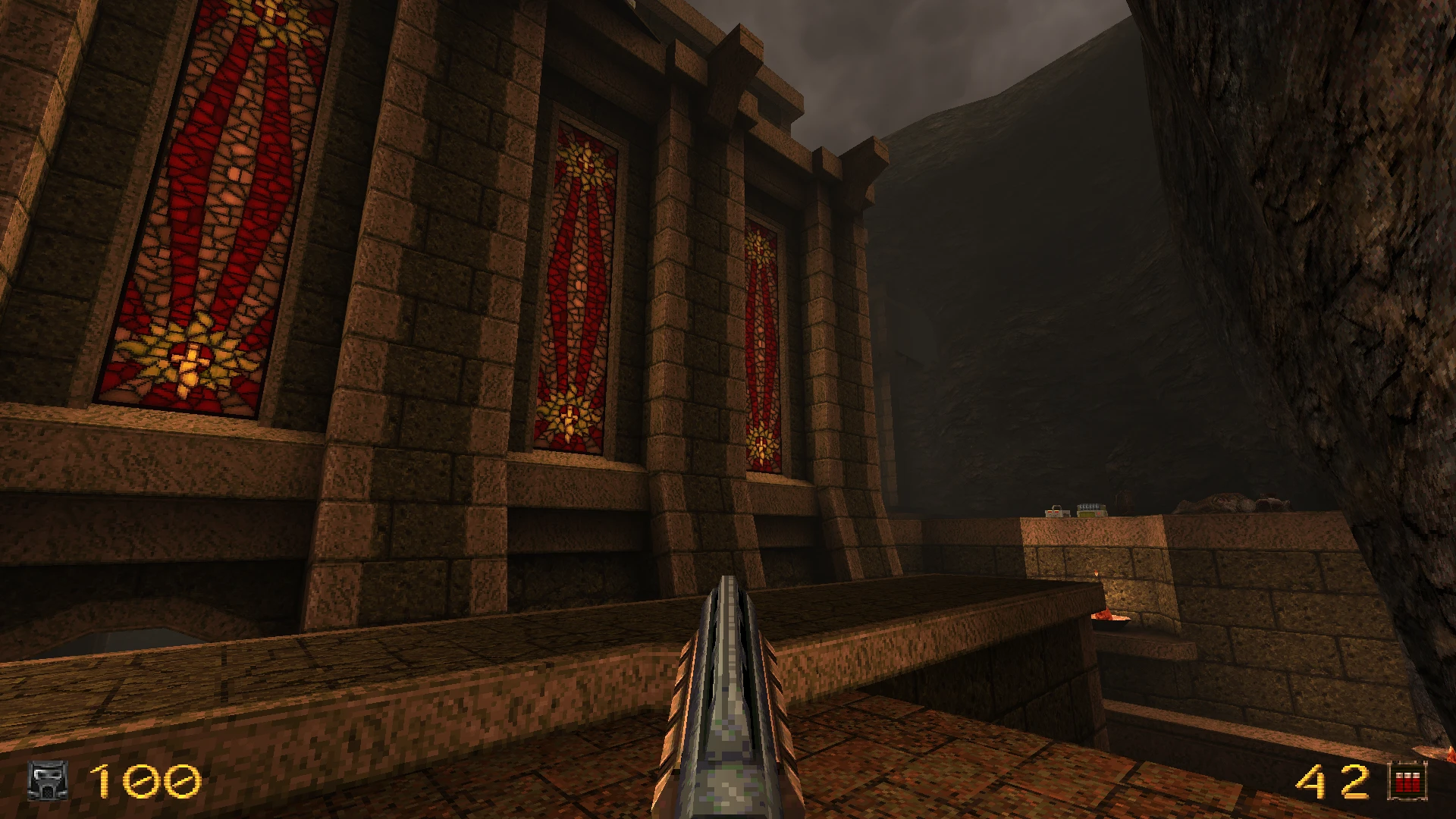 Widok z pierwszej osoby z strzelbą w modzie Quake 1996 Deathmatch Dimension pokazujący brązową kamienną architekturę i czerwone witraże